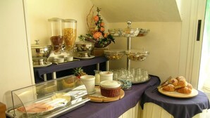 A buffet setup with various food items and containers, including a glass display case with pastries and a tiered stand with bowls of food.