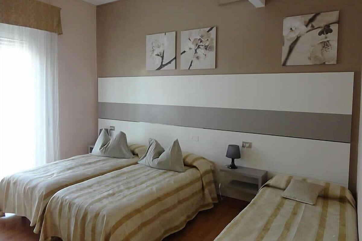 A hotel room with two beds, a nightstand, and a window with curtains.