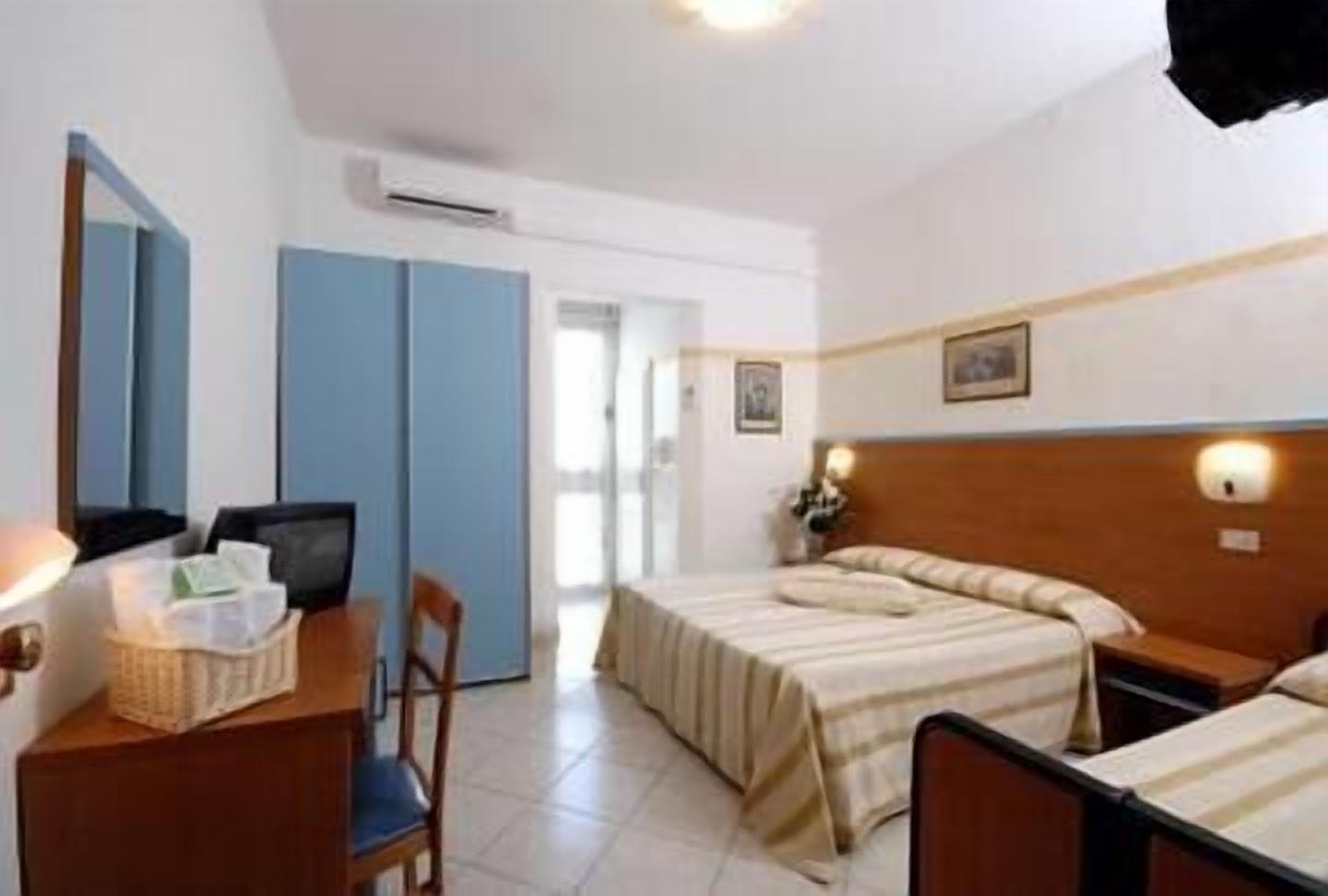 Une chambre d’hôtel avec deux lits, un bureau, une chaise, une armoire et une salle de bain visible à travers une porte ouverte.