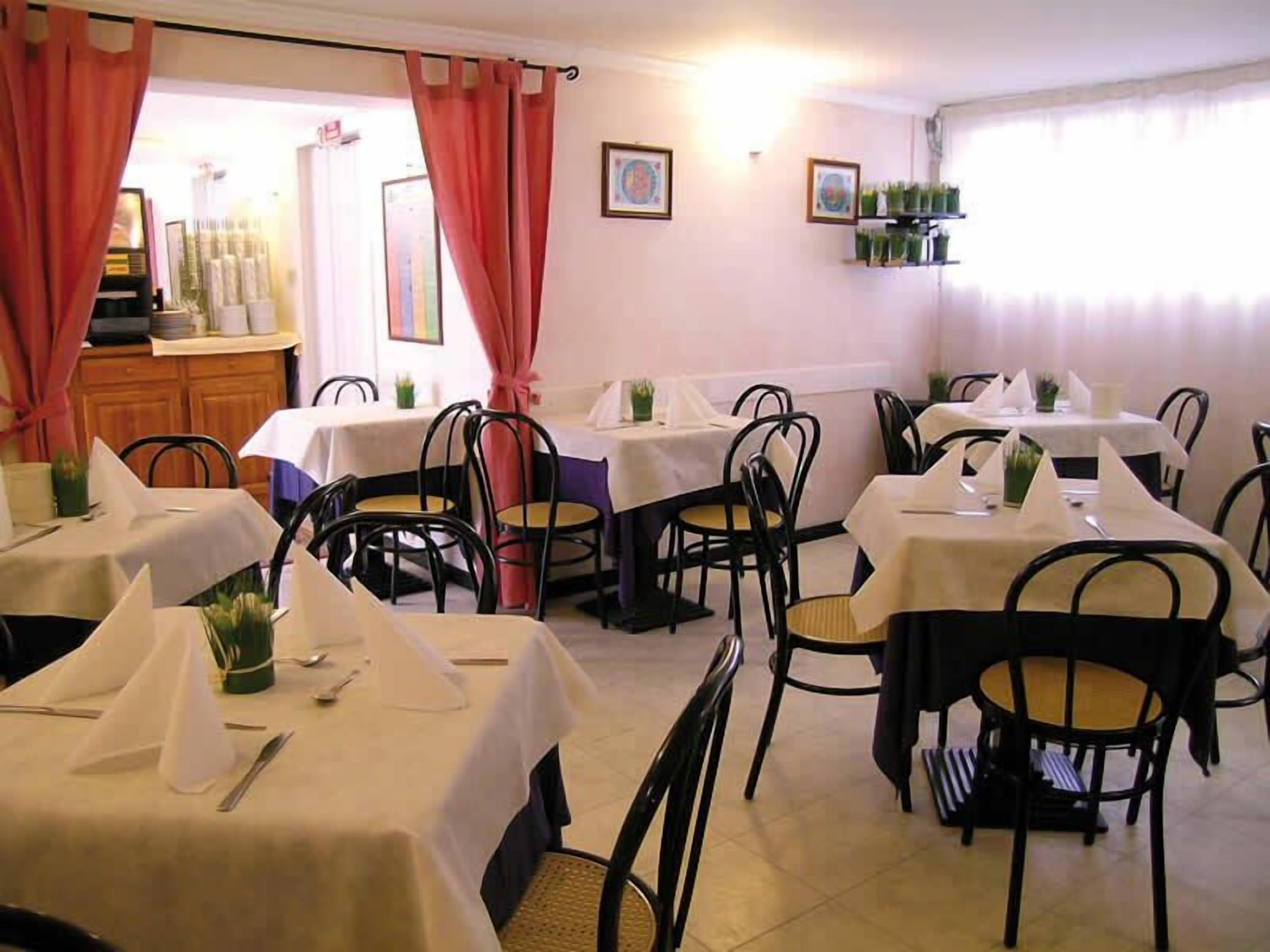Un espace repas avec des tables dressées pour quatre personnes, chacune étant recouverte d’une nappe blanche, agrémentée de chaises noires et de couverts disposés avec soin.