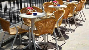 Outdoor wicker chairs and tables arranged on a tiled patio with a metal railing in the background.