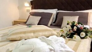 A neatly made bed with white linens, a bouquet of flowers, and a robe on the bed.