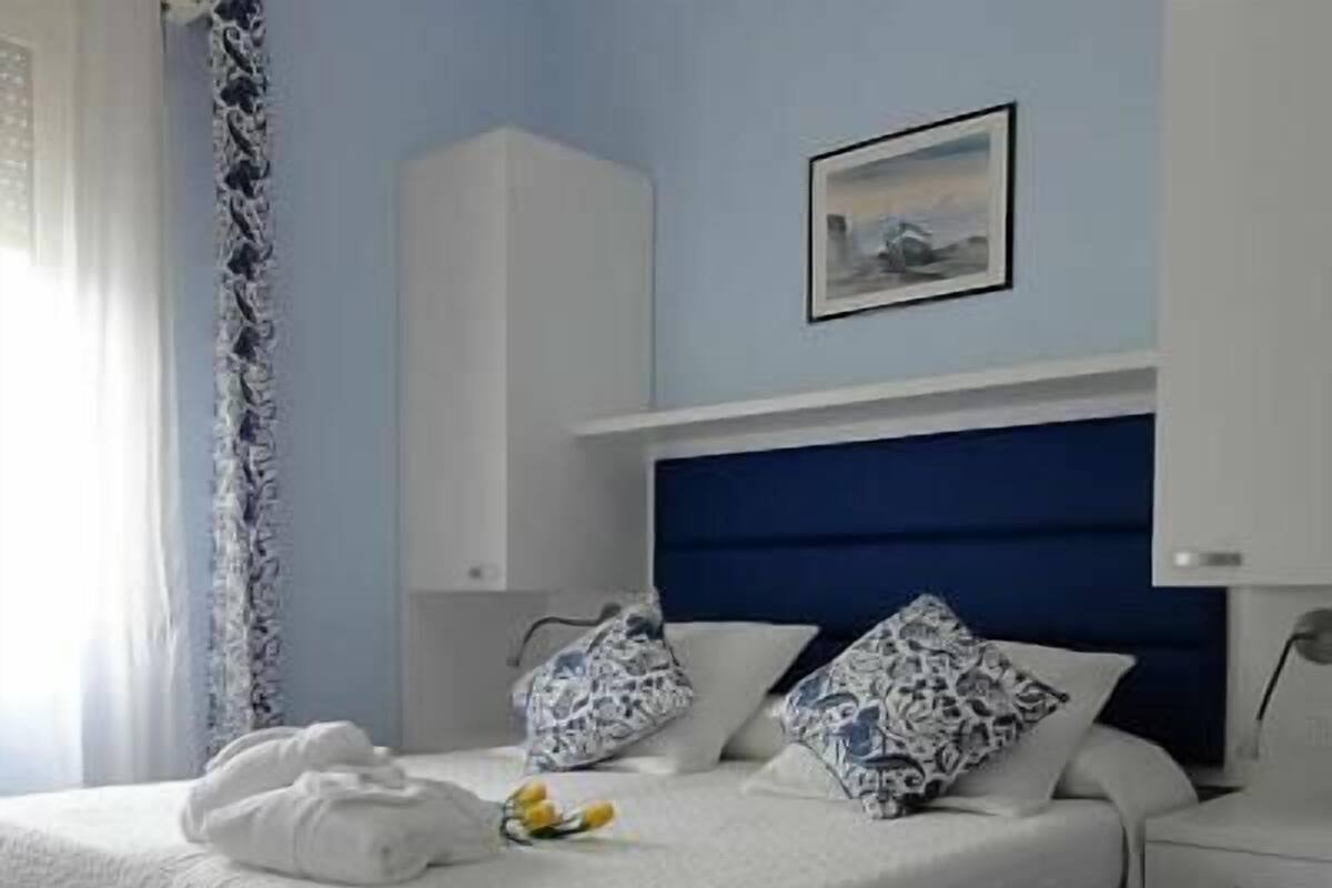 A neatly made bed with white bedding and patterned pillows, a bedside table with a lamp, and a framed picture on the wall.