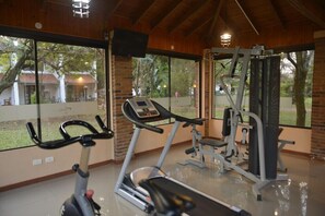 Un gimnasio con equipo de ejercicio, ventanas amplias y vistas al exterior.