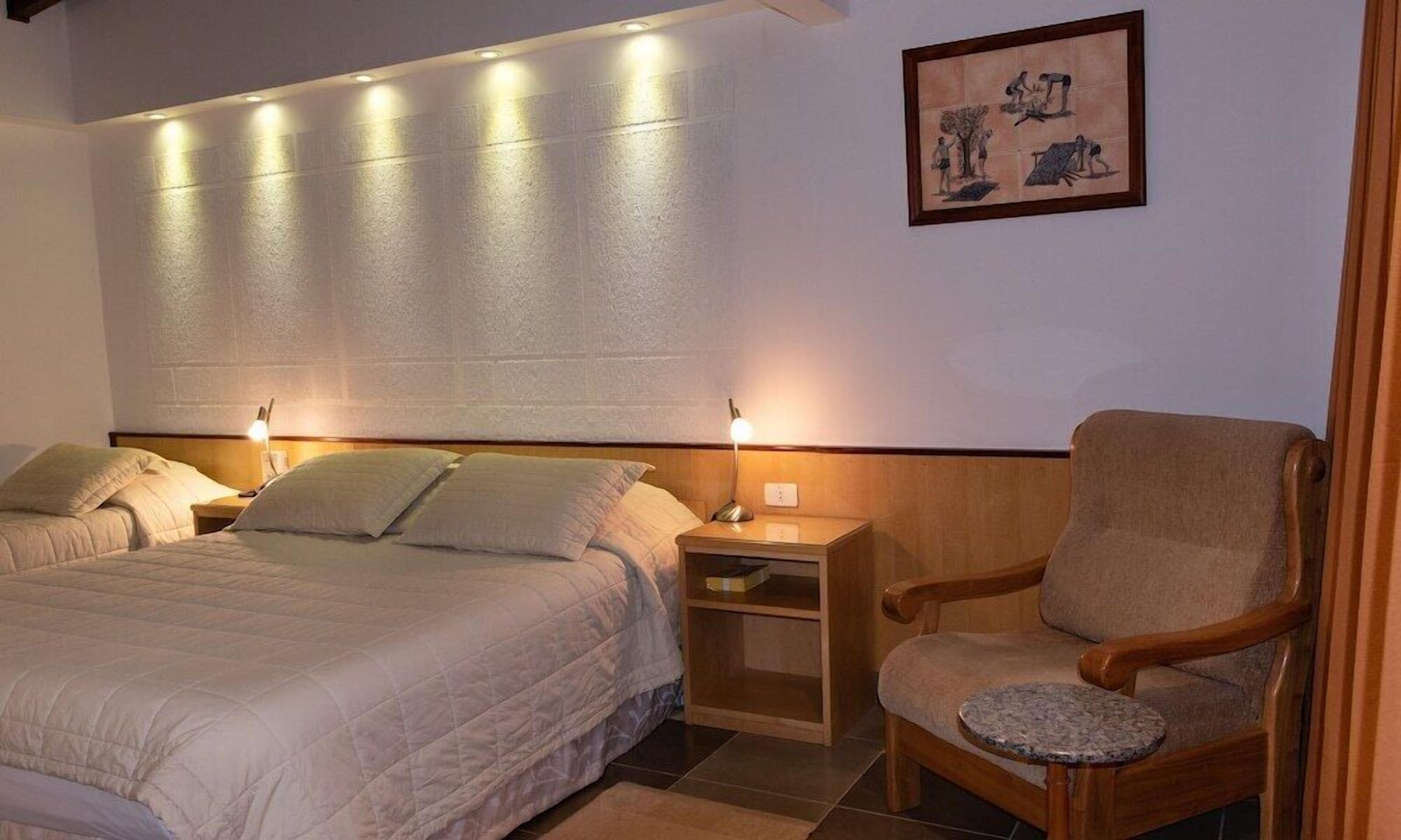 A hotel room with two beds, a wooden nightstand, a chair, and a small table.