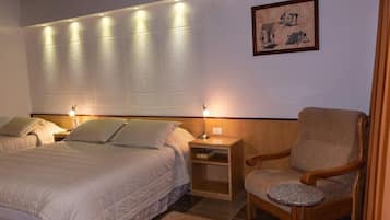 A hotel room with two beds, a wooden nightstand, a chair, and a small table.