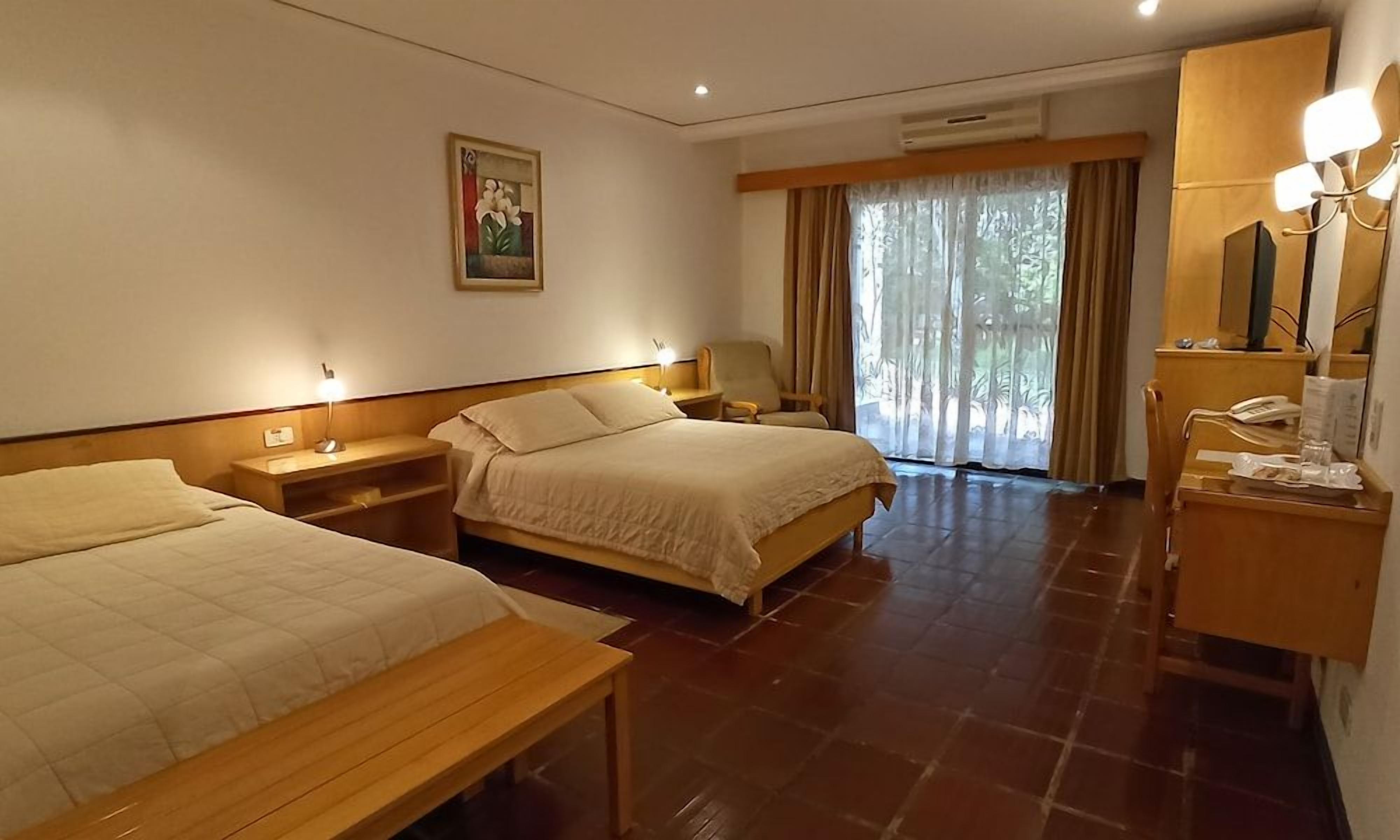 A hotel room with two beds, a desk, a chair, a mirror, and a window with curtains.