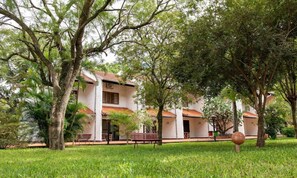A building with a white facade, multiple windows, and a red-tiled roof, surrounded by lush greenery and trees.