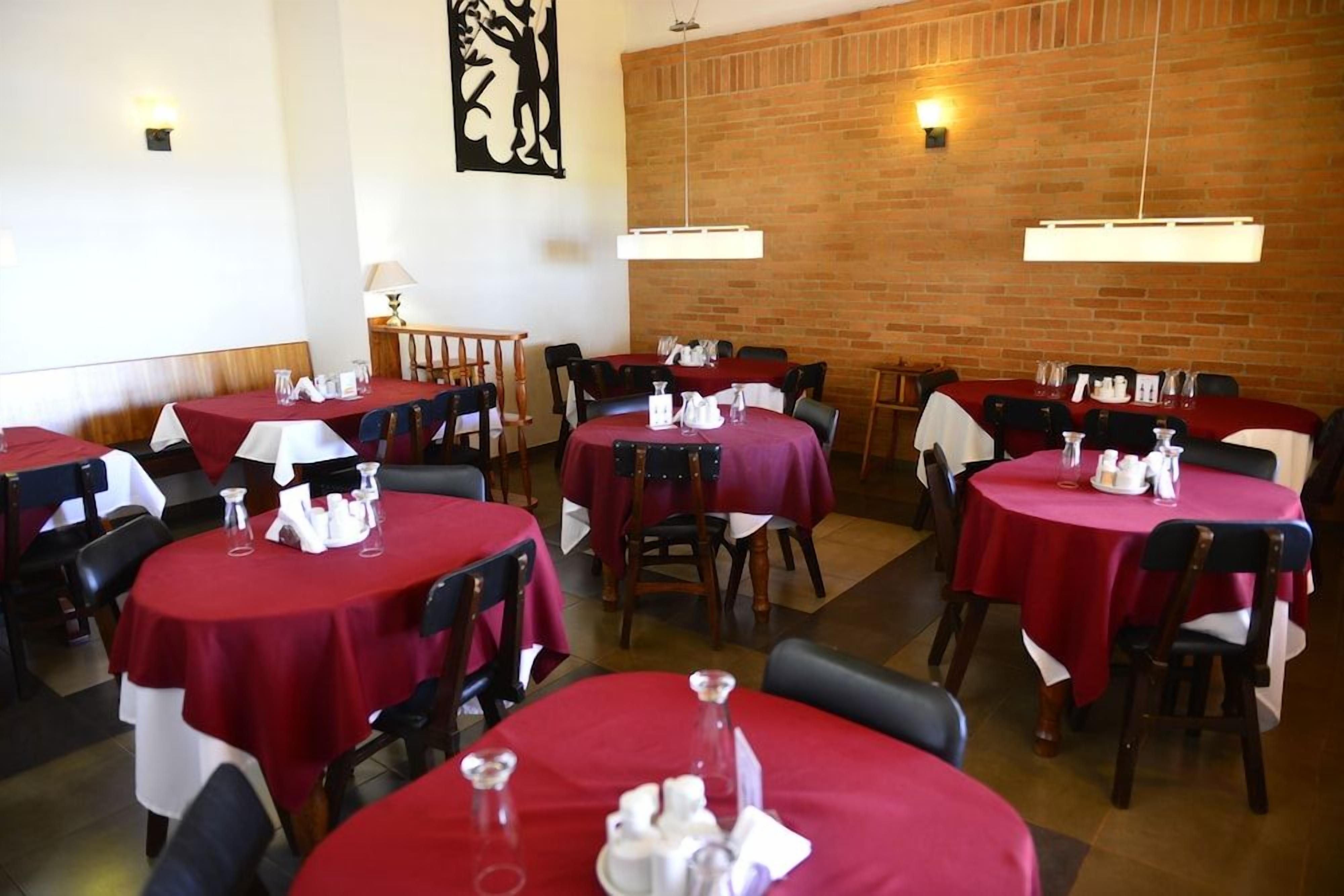 Un restaurante con mesas redondas cubiertas con manteles rojos, sillas de madera y una pared de ladrillo al fondo.