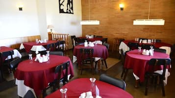 Un restaurante con mesas redondas cubiertas con manteles rojos, sillas de madera y una pared de ladrillo al fondo.