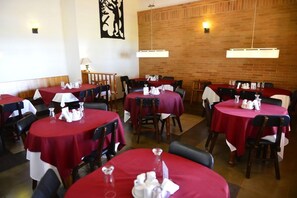 A restaurant with round tables covered in red tablecloths, wooden chairs, and a brick wall in the background.