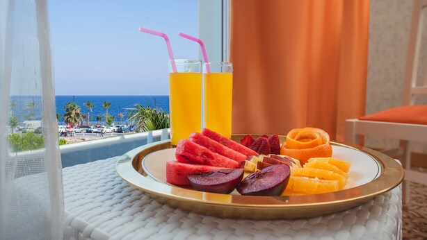 A tray with watermelon, orange slices, and a drink with a straw on a balcony overlooking the ocean. - Golden Orange Hotel (Konyaalti)