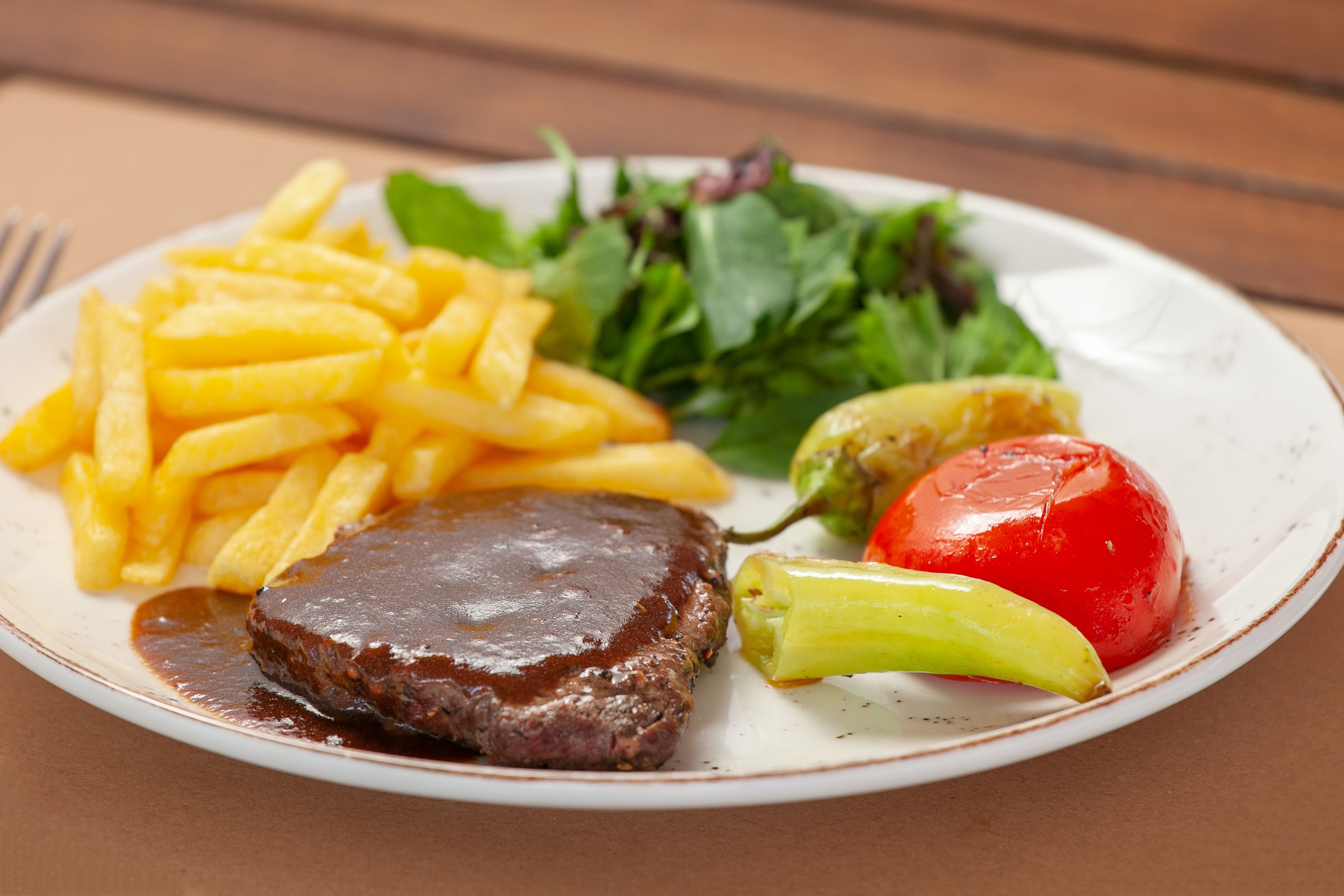 Un plato con un bistec, papas fritas, ensalada y tomate.