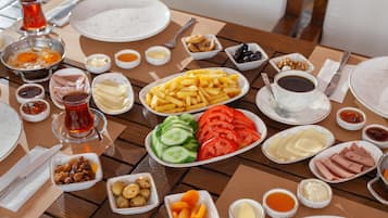 Een gedekte tafel met diverse gerechten, waaronder friet, komkommers, tomaten en vlees, samen met sauzen en drankjes.