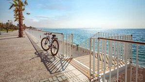 A coastal walkway with a bicycle parked by the railing, a palm tree, and a view of the sea. - Golden Orange Hotel (Konyaalti)