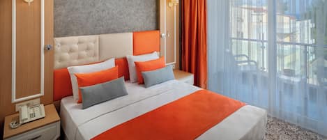 A hotel room with a bed, a telephone, a window with curtains, and a view of the outside.