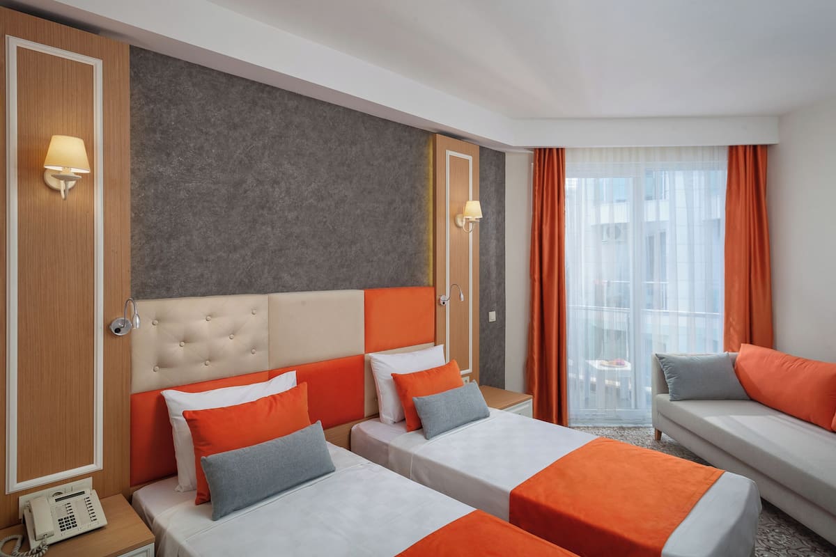 A hotel room with two beds, a sofa, a phone on the nightstand, and a window with curtains.