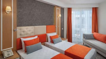 A hotel room with two beds, a sofa, a phone on the nightstand, and a window with curtains.