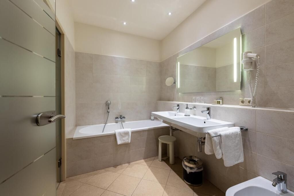 A modern bathroom with a bathtub, two sinks, a large mirror, and a bidet.