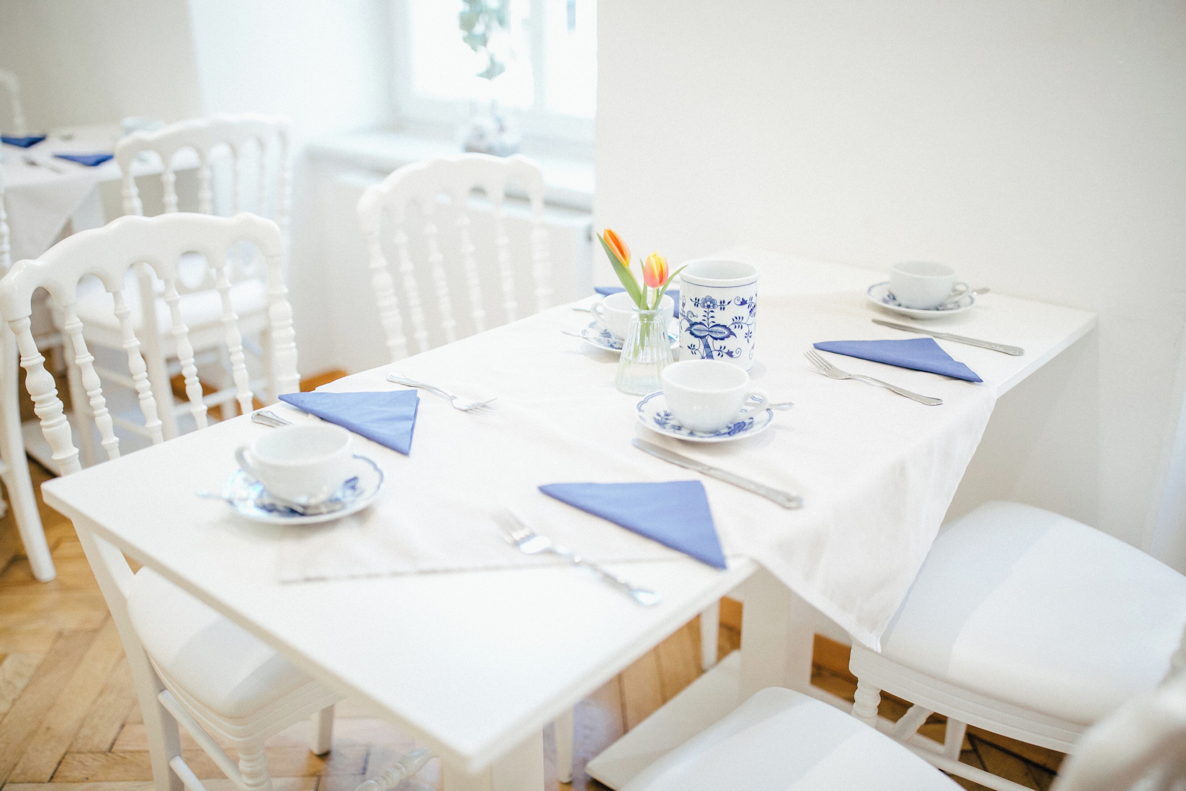 A white dining table set with blue and white plates, a vase with flowers, and silverware.