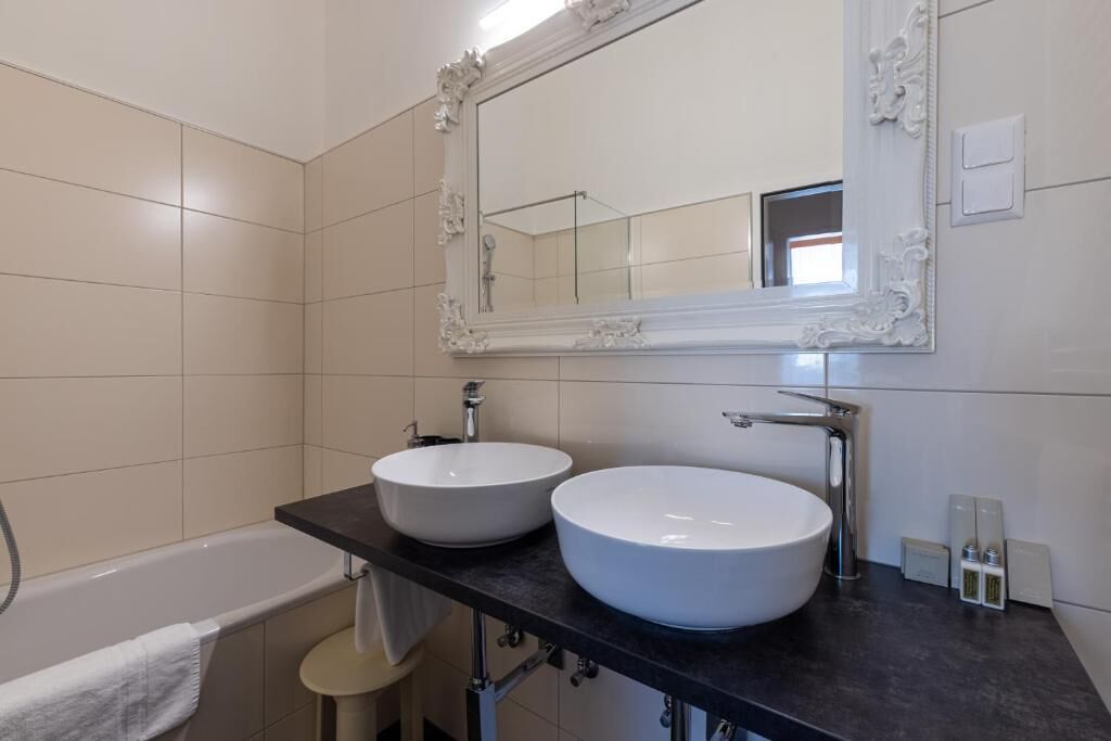 Un baño con dos lavamanos blancos, un espejo grande y una bañera.