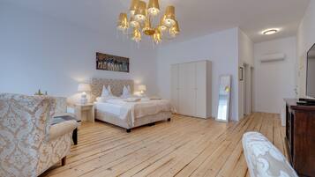 Ein Schlafzimmer mit Holzboden, einem Bett mit weißem Kopfteil, einem Nachttisch mit Lampe, einem Sessel und einem Kleiderschrank.