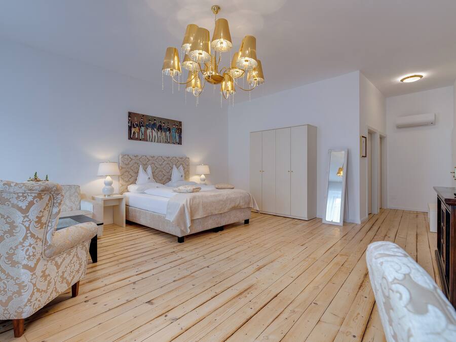 Ein Schlafzimmer mit Holzboden, einem Bett mit weißem Kopfteil, einem Nachttisch mit Lampe, einem Sessel und einem Kleiderschrank.