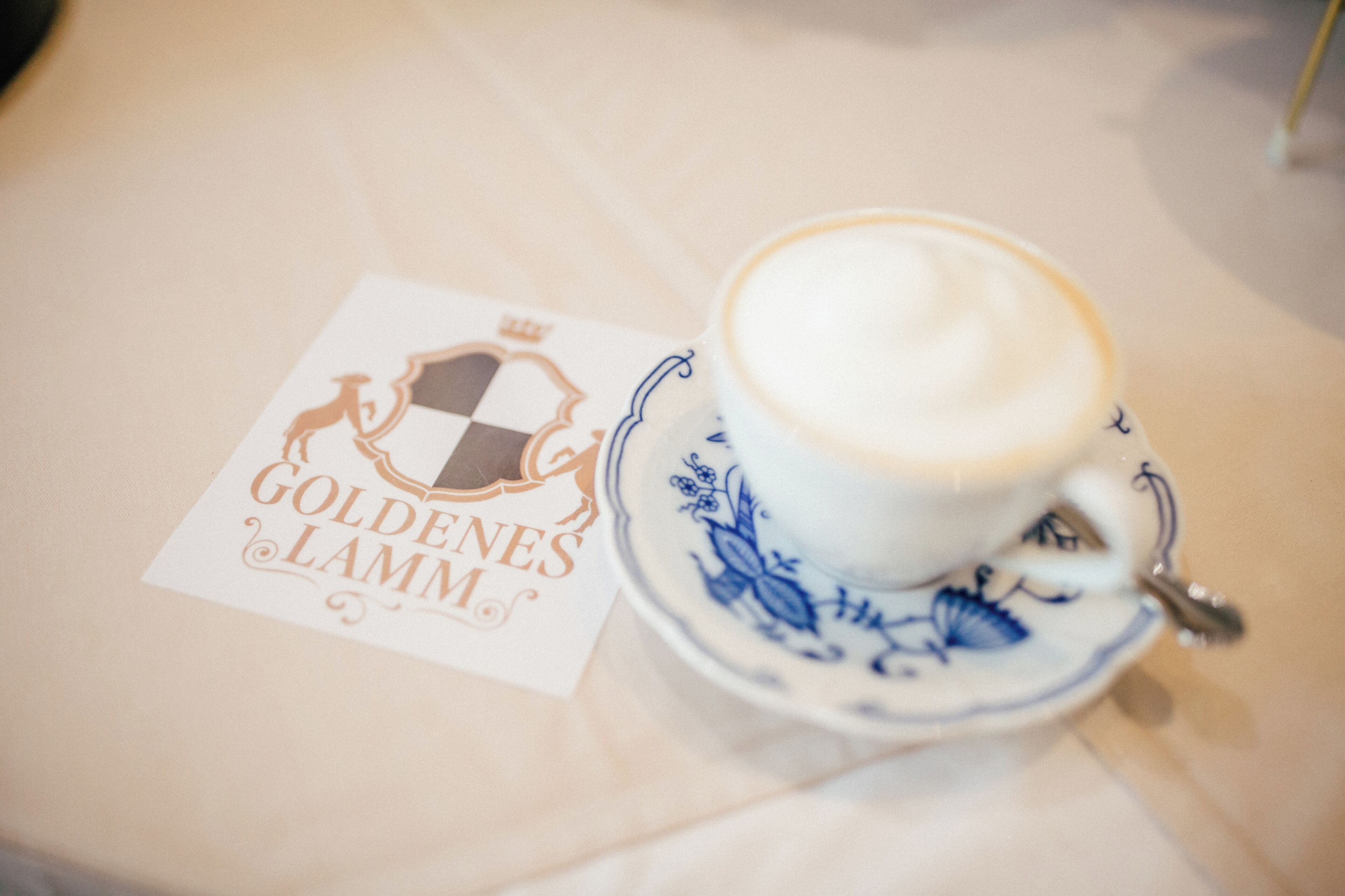 Une tasse de café posée sur une soucoupe, avec un logo et du texte imprimés sur une nappe.