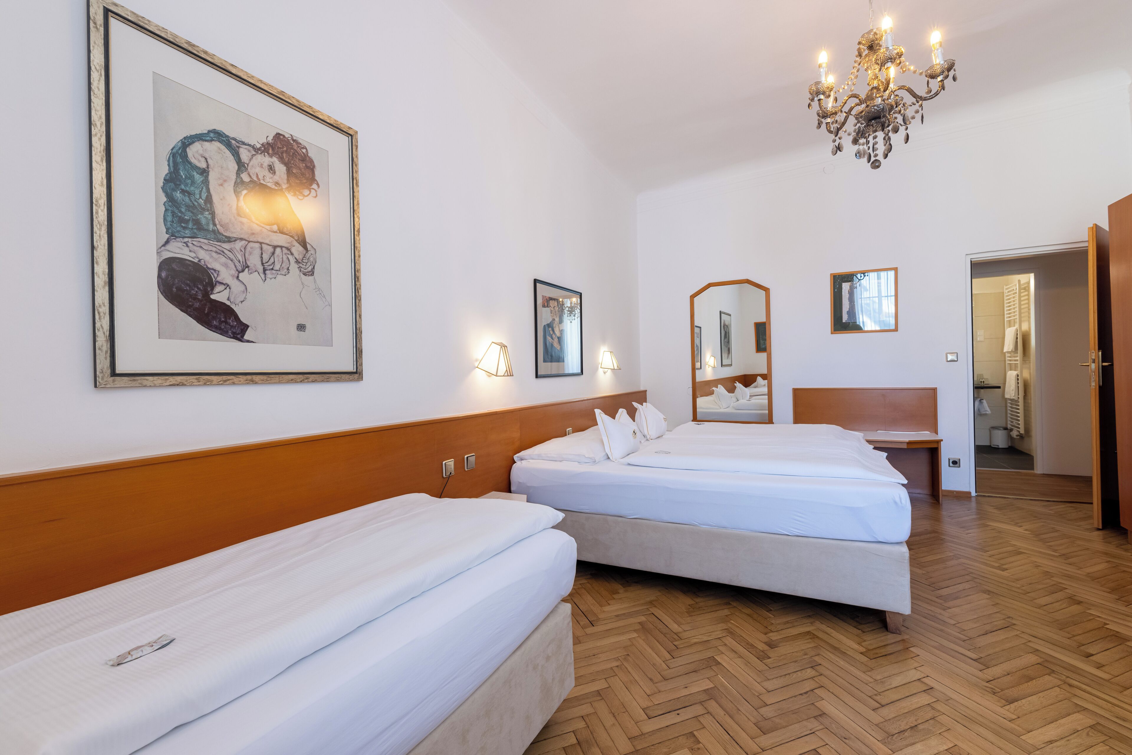 A hotel room with two beds, wooden headboards, a chandelier, and artwork on the walls.