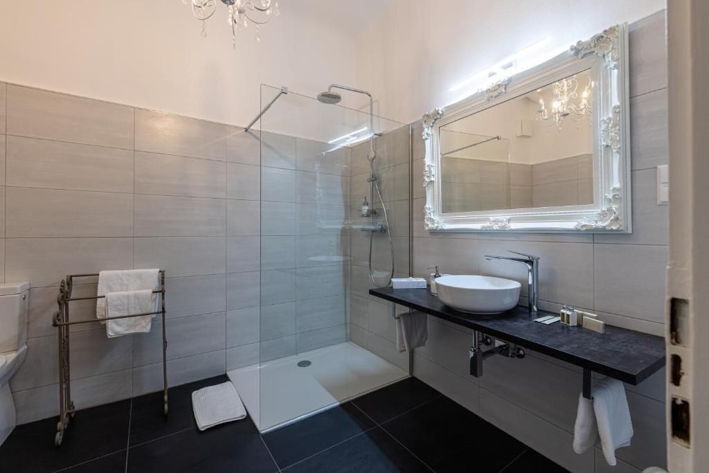 Un baño moderno con cabina de ducha de vidrio, un espejo grande y un lavabo con encimera oscura.