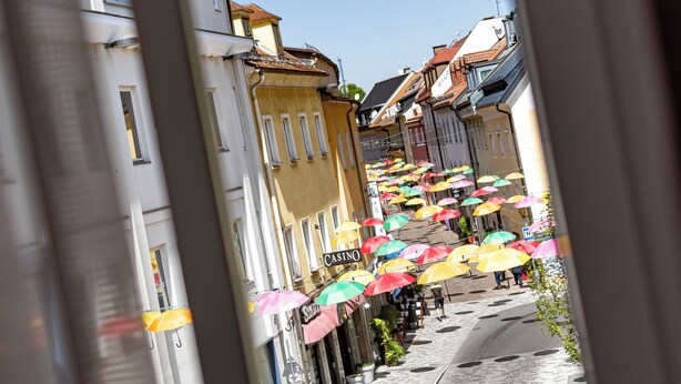 Une rue étroite bordée de bâtiments et agrémentée de parasols aux couleurs vives.