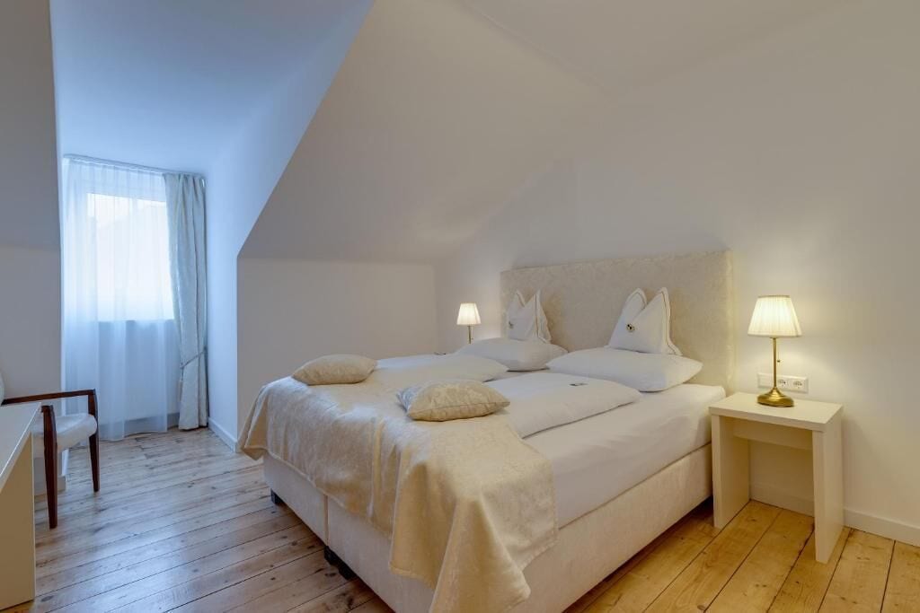 Un dormitorio con una cama grande, dos mesitas de noche con lámparas, una silla y una ventana con cortinas.