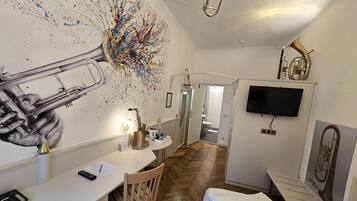 A hotel room with a desk, chair, bed, and a large abstract painting on the wall.