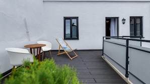 Un balcon avec un mur blanc, deux fenêtres, une chaise en bois et deux chaises blanches.
