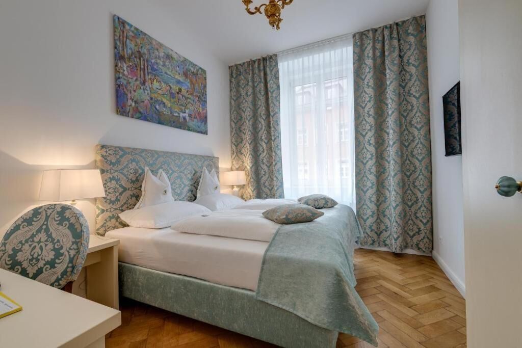 A bedroom with a bed, a nightstand, a chair, a painting on the wall, and patterned curtains.