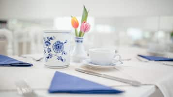 A table set with a white tablecloth, a blue and white floral mug, a white cup and saucer, a vase with tulips, and a blue napkin.