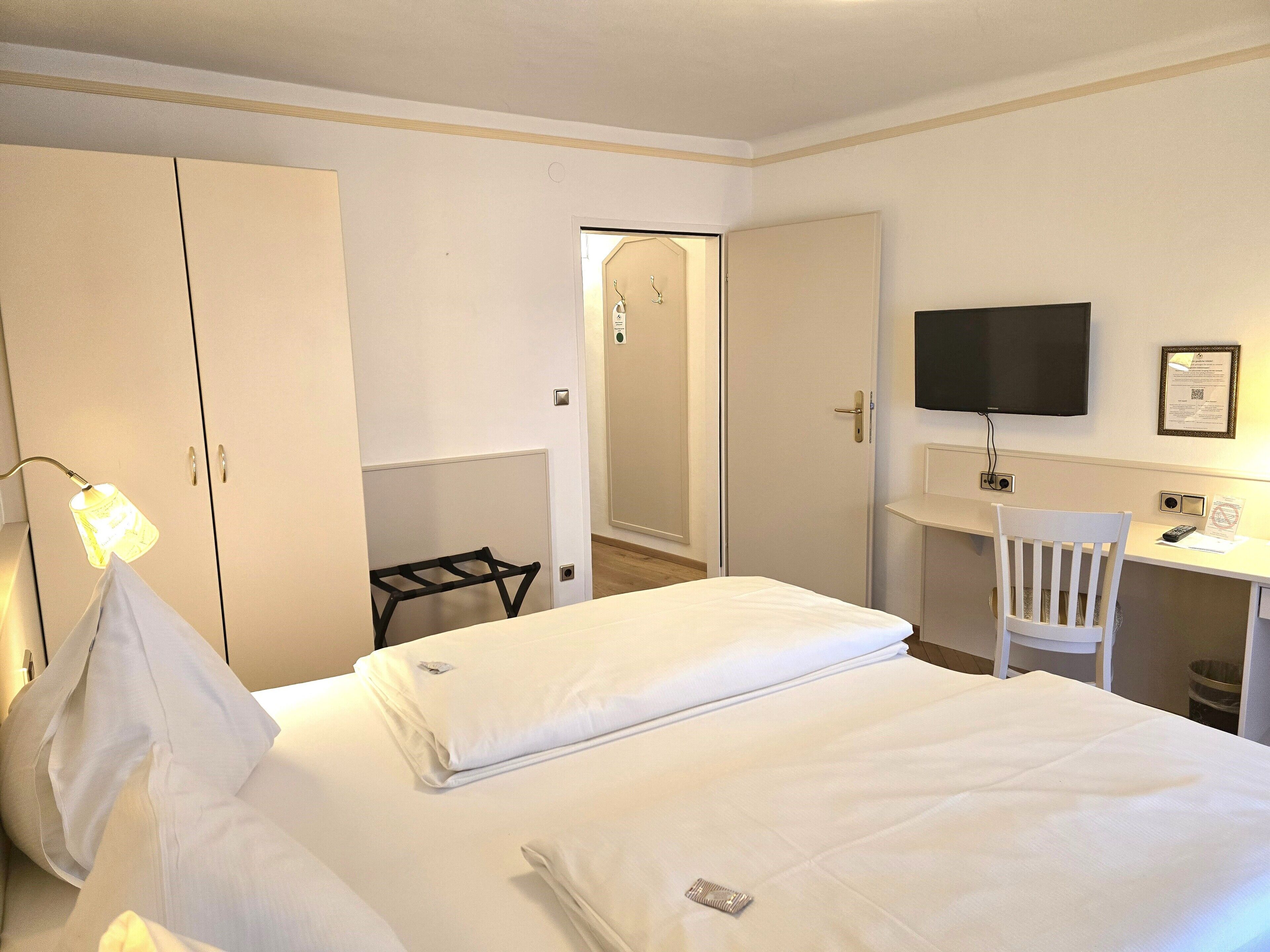 A hotel room with a bed, a desk, a chair, a TV, and a wardrobe.
