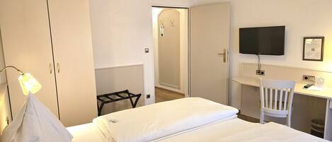 A hotel room with a bed, a desk, a chair, a TV, and a wardrobe.