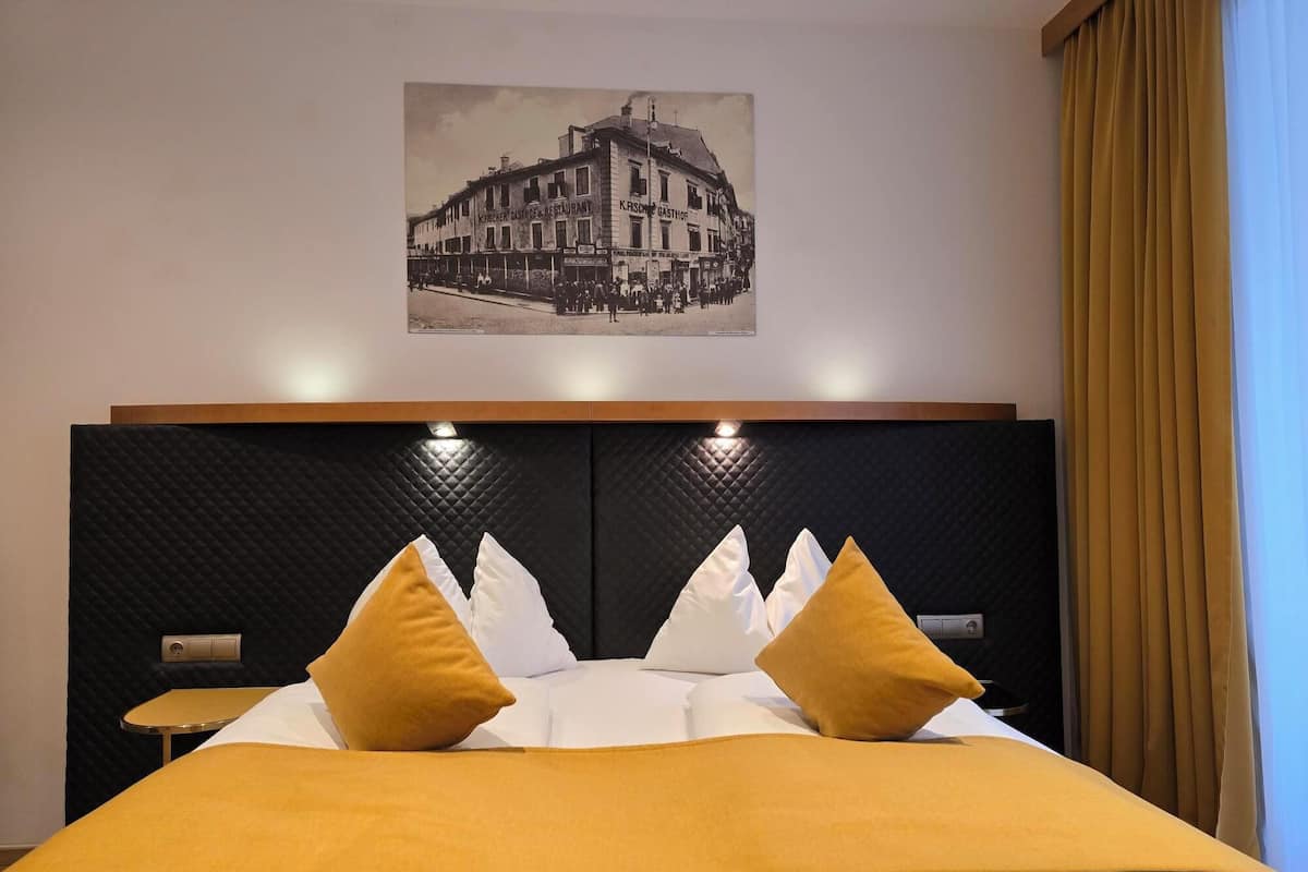 Ein Hotelzimmer mit einem großen Bett, zwei Nachttischen, einem Kopfteil mit integrierter Beleuchtung und einem gerahmten Foto an der Wand.