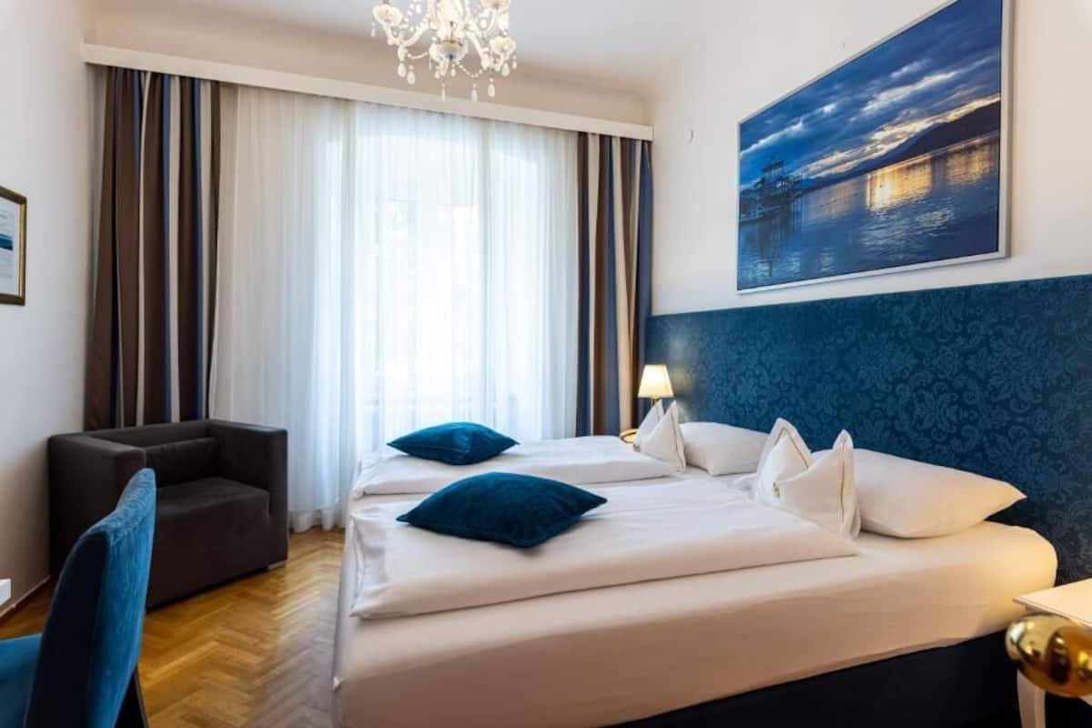 Ein Hotelzimmer mit einem großen Bett, einem Sessel, einem Schreibtisch und einem Gemälde einer Nachtszene.