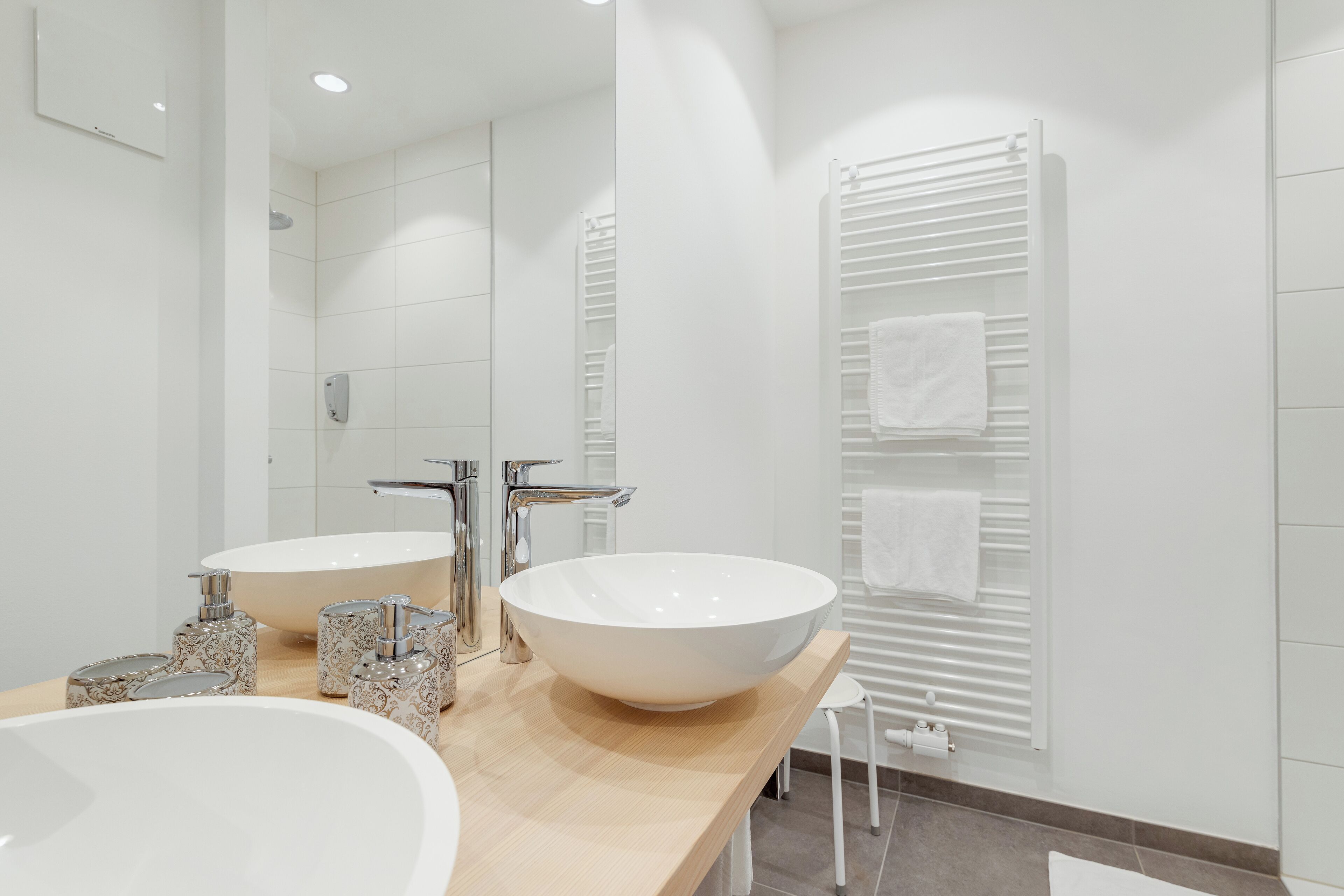Ein modernes Badezimmer mit zwei großen weißen Waschbecken, einem Spiegel und einem Handtuchhalter.