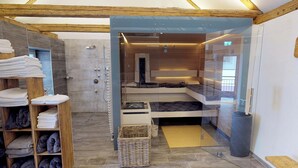 Une salle de bain moderne dotée d’une douche à parois de verre, d’une étagère en bois où sont posées des serviettes et d’un banc intégré avec espace de rangement.