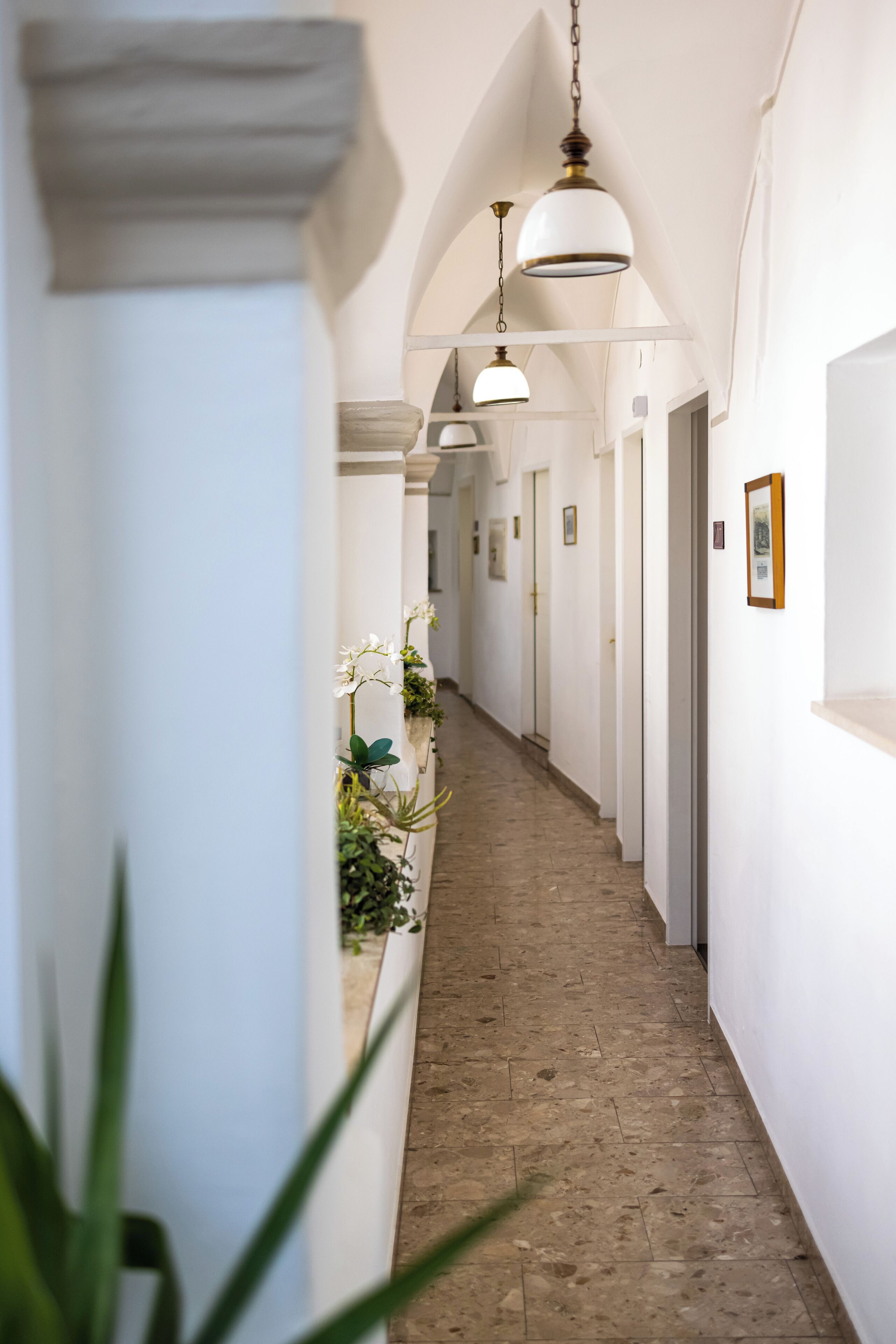 A hallway with white walls, a tiled floor, and hanging pendant lights.