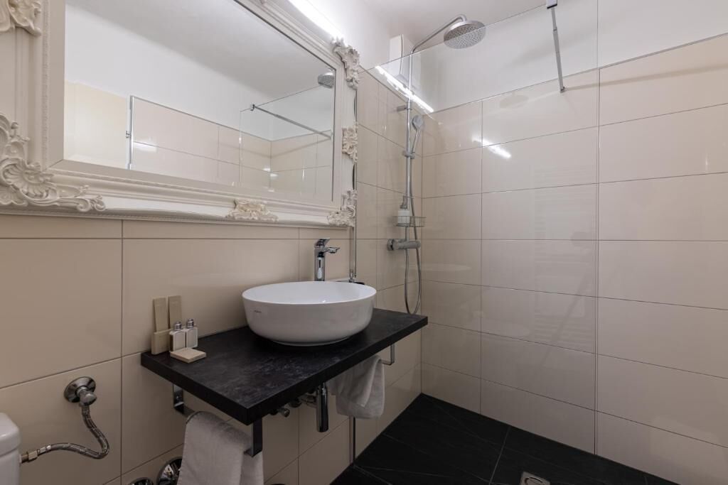 Une salle de bain moderne avec un lavabo blanc, un plan de toilette noir et un grand miroir aux motifs décoratifs élaborés.