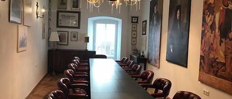 Un salón de conferencias con una larga mesa y sillas, una araña, cuadros enmarcados y un cuadro grande en la pared.