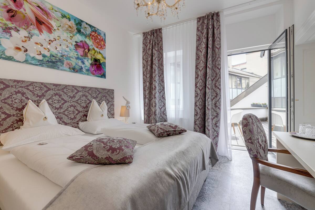 Ein Schlafzimmer mit einem großen Bett, einem Schreibtisch und einem Stuhl. Es gibt ein Fenster mit Vorhängen und Blick nach draußen.
