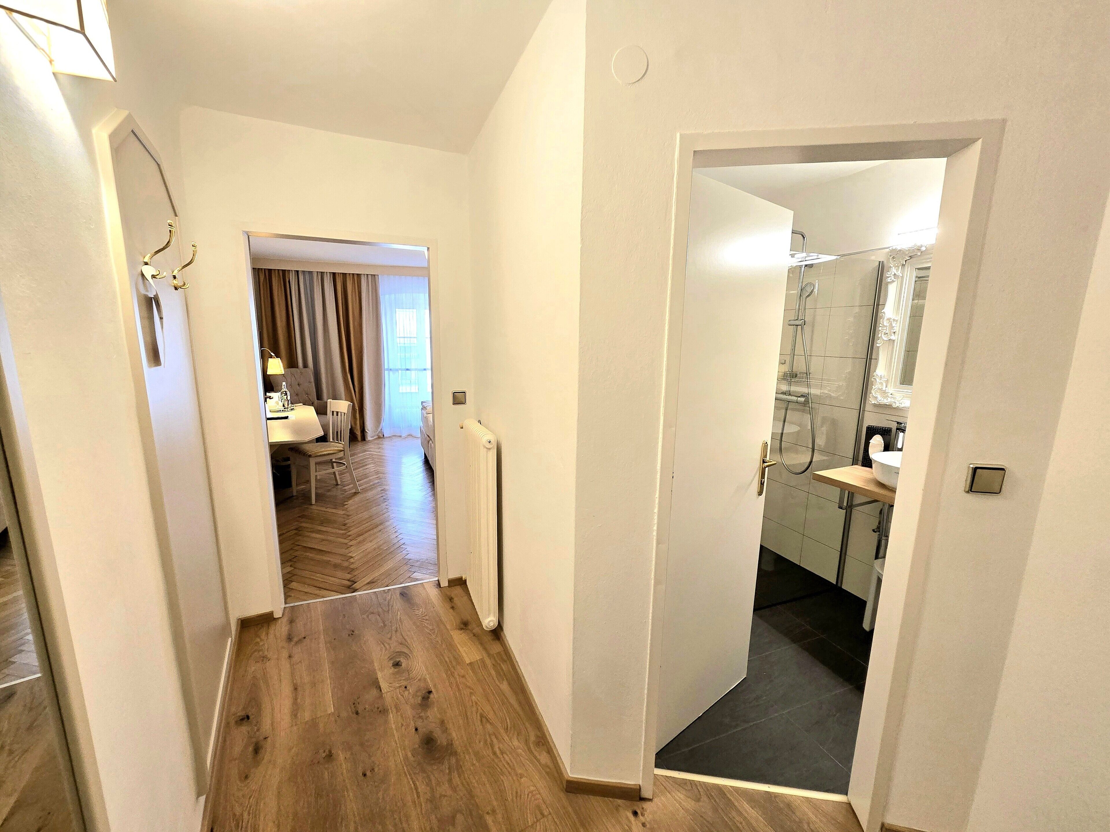 Un pasillo con suelo de madera que conduce a un baño con ducha y lavamanos.