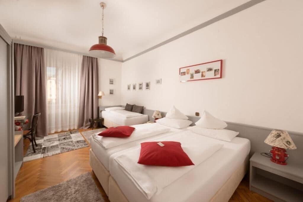 Een hotelkamer met twee bedden, een bureau, een stoel, een televisie en een rode lamp.
