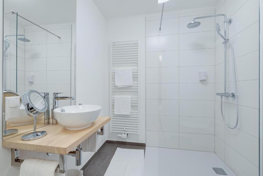A modern bathroom with a large mirror, a white sink, and a glass-enclosed shower area.