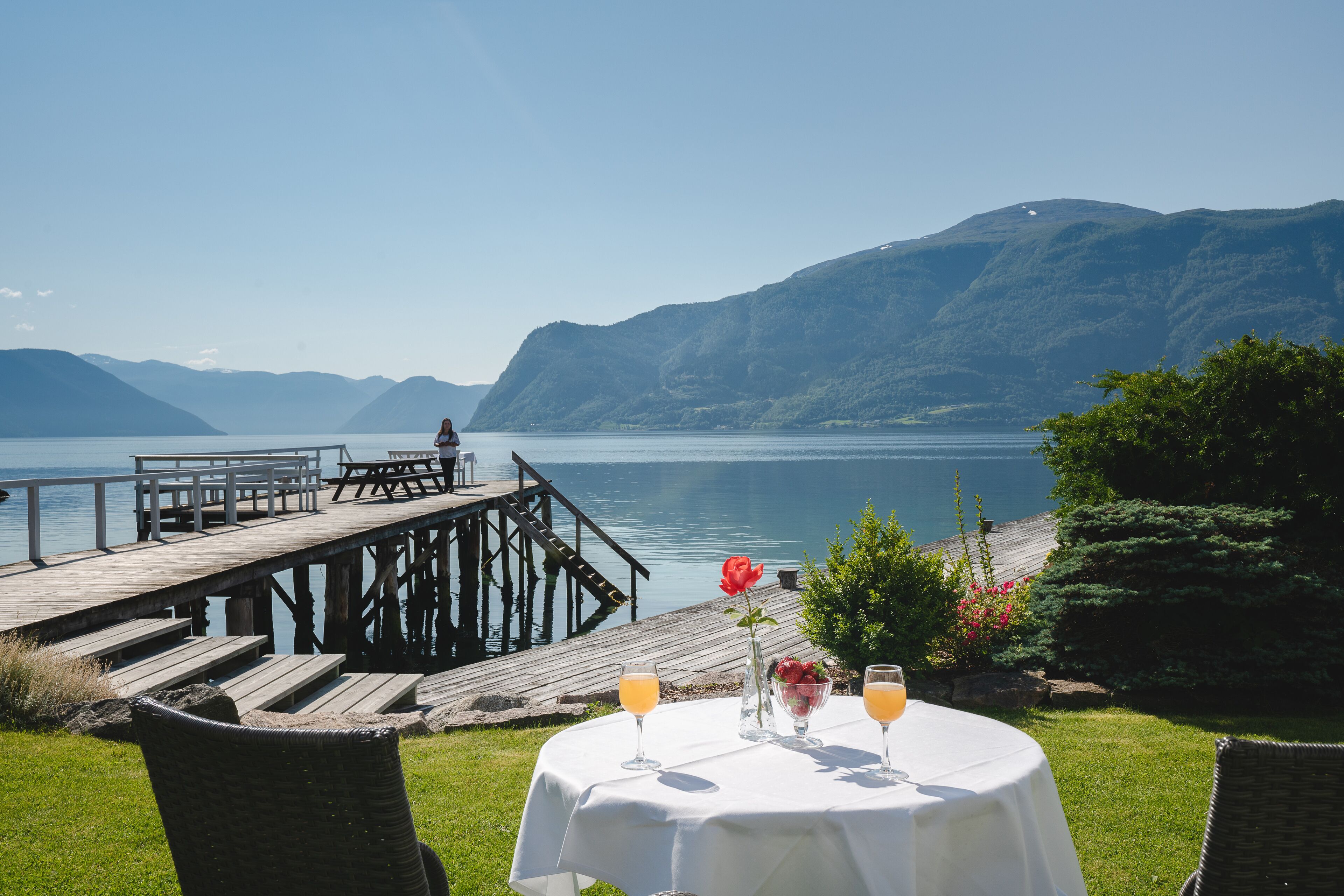 A lakeside dining area with a table set for two, overlooking a calm lake and mountains.
